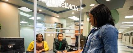一名学生站在招生服务台前，与桌子另一边的两名特拉华理工大学员工交谈