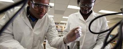 两个学生穿着实验服，戴着护目镜在实验室里做实验